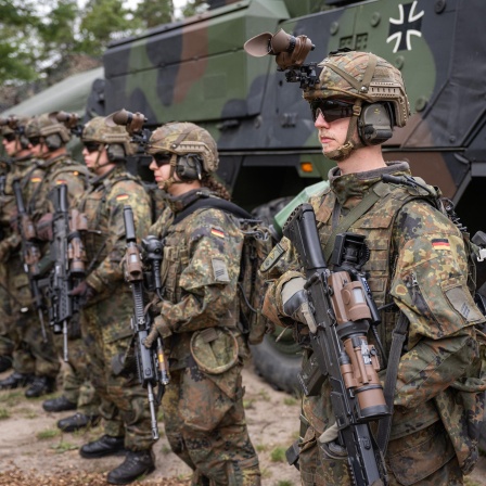 Bewaffnete Grenadiere stehen auf einem Bundeswehrgelände vor einem Militärfahrzeug.