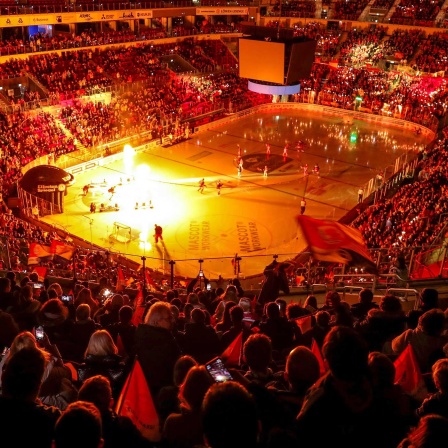 Eishockey-Fans in der vollen Eishalle. Auf dem Spielfeld laufen die Mannschaften mit einer Riesenshow ein (Bild: picture alliance / Maximilian Koch)