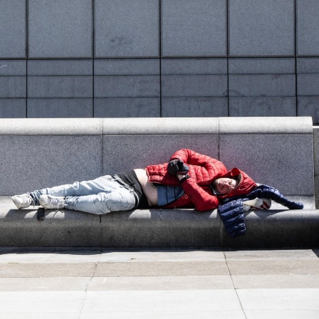 Zwei obdachlose Männer schlafen in San Franzisko auf einer Beton-Bank.