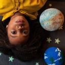 Ein Kind liegt auf dem Boden neben gebastelteten Planeten und Sternen.