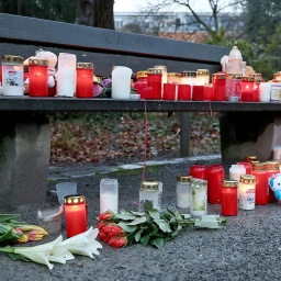 Trauerkerzen, Blumen und Kuscheltiere liegen in einem Park auf einer Bank.