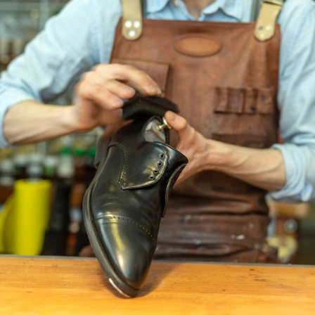 Ein Schuhmacher poliert Schuh in der Werkstatt.