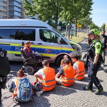 Polizisten stehen um Mitglieder der Protestgruppe Letzte Generation nach einer Sitzblockade auf dem Leipziger Georgiring