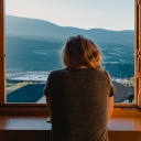 Eine junge Frau schaut aus dem Fenster auf eine Berglandschaft.