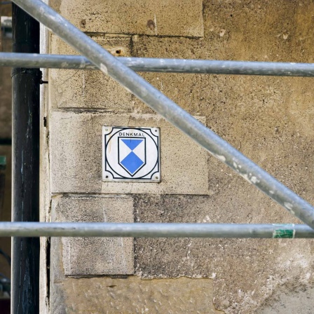 Ein Baugerüst an einem Gebäude, auf dem ein Emblem mit der Aufschrift Denkmal angebracht ist.