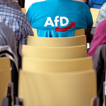 Ein Mann mit einem T-Shirt mit AfD-Logo sitzt während des Landesparteitags der Alternative für Deutschland Hessen im Haus der Begegnung im Publikum.