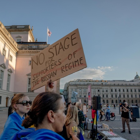 Eine Frau hält vor der Staatsoper Berlin ein Schild mit der Aufschrift "No stage for supports of the Russian regime" hoch, als Protest gegen den Auftritt von Anna Netrebko.