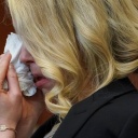 Nahaufnahme von Amber Heard im Gerichtssaal, die sich, halb von ihrem blonden Haar verborgen, Tränen mit einem Taschentuch abwischt.