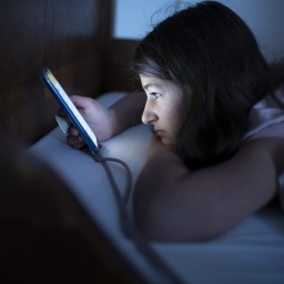 Ein Mädchen schaut im Dunkeln auf ihr Smartphone, während sie im Bett liegt