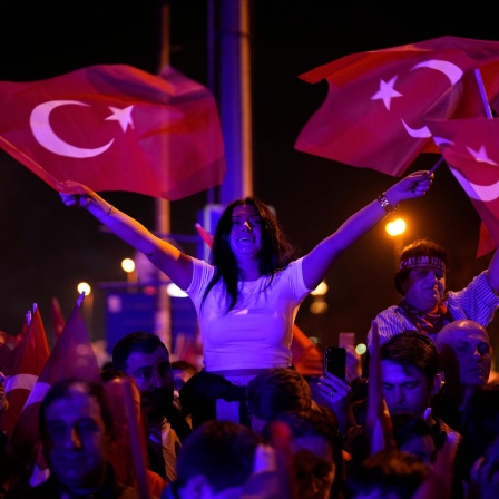 Eine Frau jubelt mit zwei Türkei-Fahnen in ihren Händen.