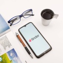 Ein Tisch mit einem Magazin, einem Stift, einer Briller und einem Smartphone auf dem Tinder zu sehen ist.