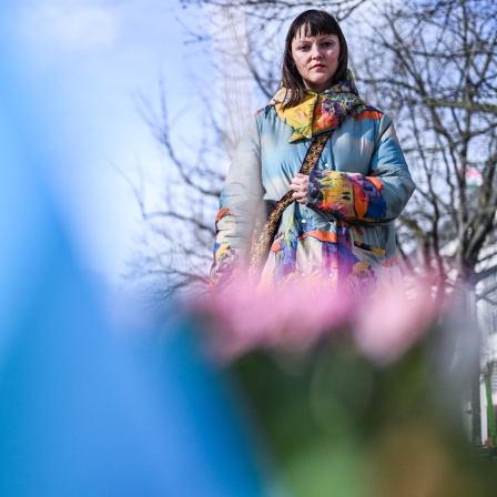 Eine Frau schaut auf Blumen und eine ukrainische Flagge, die im Vordergrund in der Unschärfe zu sehen sind.