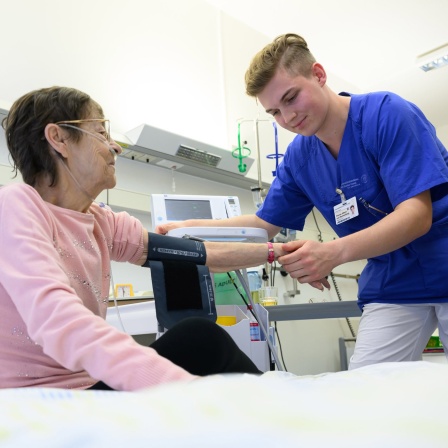 Ein junger Mann misst bei einer Patientin Blutdruck. Symbolbild: Pflegeausbildung
