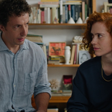 Szene aus dem Film "Volveréis - Ein fast klassischer Liebesfilm": Ein Mann und eine Frau sitzen nebeneinander und schauen sich skeptisch an.