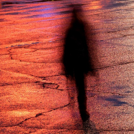Der Schatten einer Frau auf einer beleuchteten Straße lässt sie wie ein Geist erscheinen.