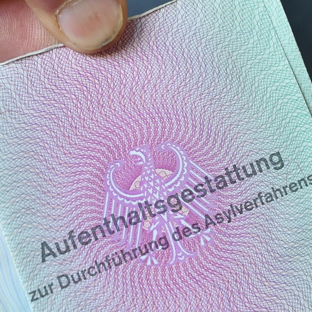 Ein Mann aus Syrien zeigt in der Gemeinschaftsunterkunft für Geflüchtete seine Aufenthaltsgestattung