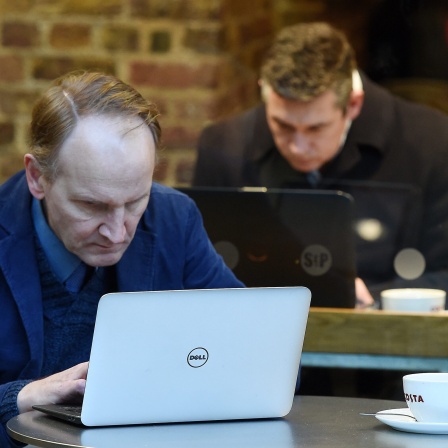 Zwei Männer arbeiten an Laptops in der Filiale einer Kaffee-Kette und belegen damit zwei Tische.