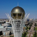 Eine Luftansicht von Nur Sultan in Kasachstan. Futuristische Hochhäuser und im Vordergrund ein Monument mit grosser goldener Kugel auf der Spitze.