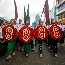 Mädchen in Hochschul-Uniformen tragen vier Blumengestecke jeweils mit der Ziffer Acht die Straßen von Yangon.