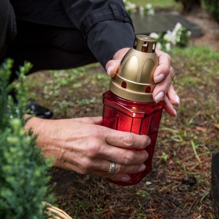 Eine Frau zündet in Hamburg auf einem Friedhof eine Kerze an.