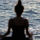 Silhouette einer Frau, die am Meer meditiert.