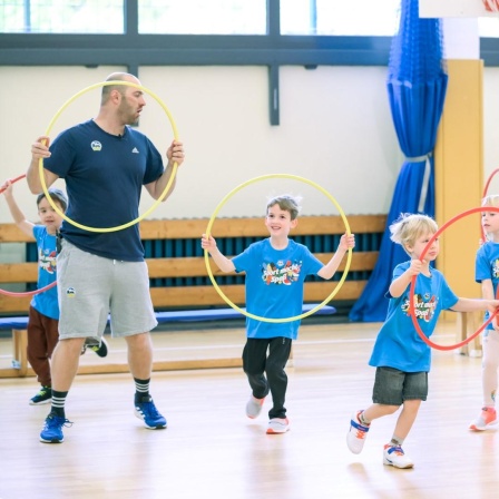 Ein Trainer zeigt den Kindern Übungen mit dem Hula-Hoop-Reifen.