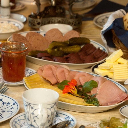 Eine üppig gedeckte Bergische Kaffeetafel mit Rosinenstuten, Wurst, Schinken, Käse, Birnenkraut, Apfelkraut, Quark, Butter und Kirschen.