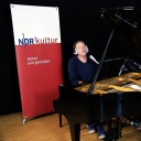 Der Musiker Jens Thomas trägt im Studio von NDR Kultur ein Lied an einem Flügel vor.