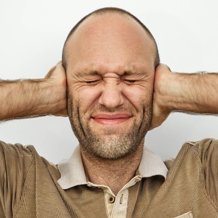 Ein Mann hält sich mit geschlossenen Augen gestresst die Ohren zu: Stresserfahrungen werden in der Großhirnrinde als Gedächtnisspuren abgelegt