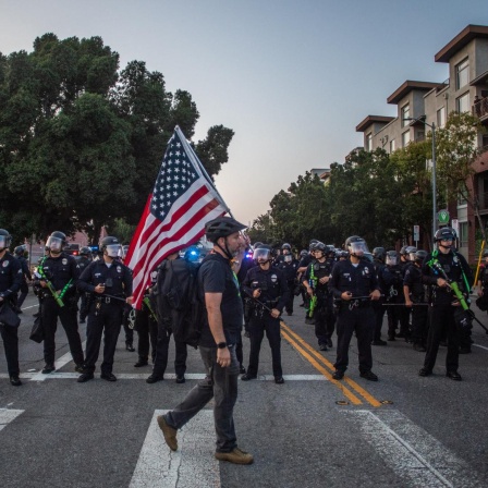Ein Mann mit US-Flagge läuft in Los Angeles an Polizisten vorbei