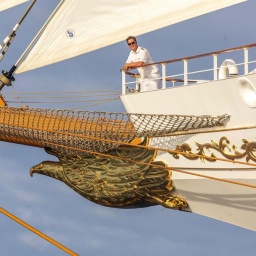 Der Kapitän Heiner Eilers steht auf dem Bug des Segelschiffs Sea Cloud Spirit und lächelt in die Kamera.