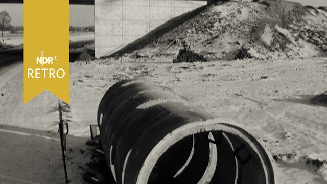 Rohrelemente vor einer Brücke am Rand einer im Bau befindlichen Autobahn (1963)