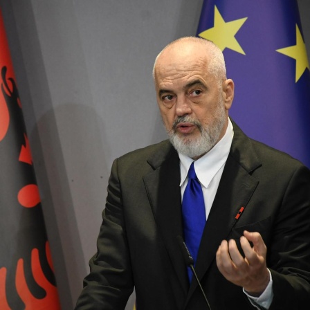 Edi Rama steht vor der albanischen und der europäischen Flagge und spricht.