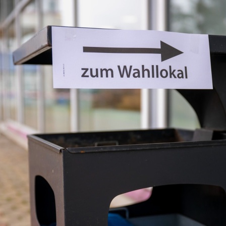 Auf einem öffentlichen Mülleimer ist ein Hinweisschild angebracht, dass die Richtung zu einem Wahllokal anzeigt.