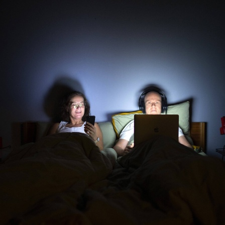 Paar liegt mit ihren technischen Geräten im Bett