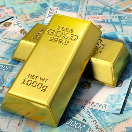 Goldbarren liegen auf Geldscheinen.