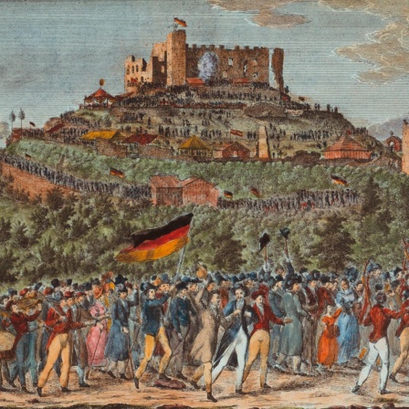 Das Bild aus dem Jahr 1832 zeigt eine Panorama-Perspektive auf das Schloss Hambach mit einem langen Menschenzug, der darauf zuhält. Die Leute schwenken Fahnen in den Farben Schwarz-Rot-Gold.