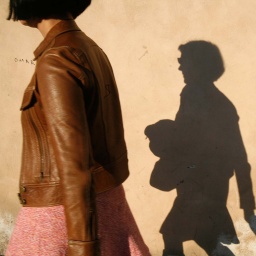 Frau läuft vor Wand entlang mit Schatten einer anderen Frau