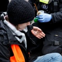 Eine junge Aktivistin der 'Letzten Generation' hat sich in Berlin auf einer Strasse festgeklebt, ihre Hände zeigen die Sekundenkleberspuren während ein Polizist sie losmacht, Dezember 2022.