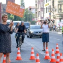 Eine Aktivistin zeigt auf der Karl-Marx-Straße ein Schild mit der Aufschrift "Stoppt Falschparker". Der Verkehrsclub Deutschland VCD und die Initiative Clevere Städte richteten zur bundesweiten Falschparker-Woche einen Not-Radweg ein, der durch die rot-weißen Verkehrshütchen markiert wird.