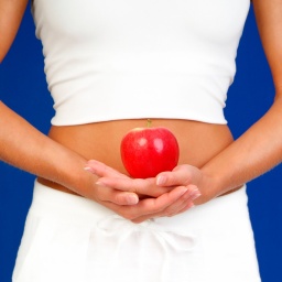 Frau hält Apfel vor Bauch