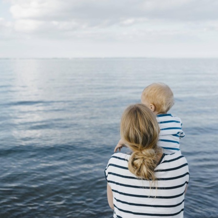 Eine Mutter steht mit ihrem jungen Sohn am Meer.