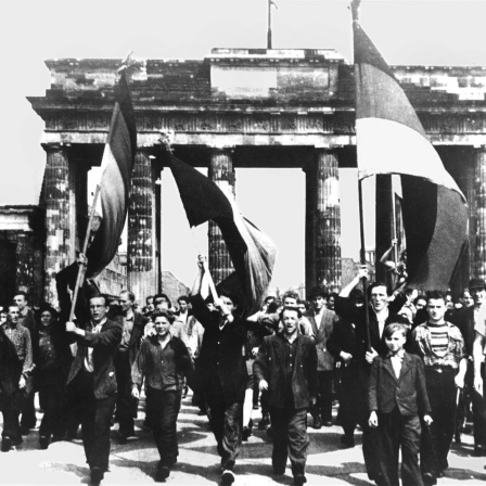 Ost-Berliner marschieren am 17 Juni 1953 mit wehenden Fahnen vom Ost-Sektor aus durch das Brandenburger Tor. Nach Streiks in Ost-Berlin kam es zum Volksaufstand, der von sowjetischen Truppen niedergeschlagen wurde.