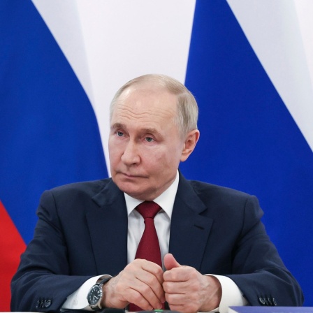 Wladimir Putin mit ernstem Gesichtsausdruck vor russischen Fahnen 