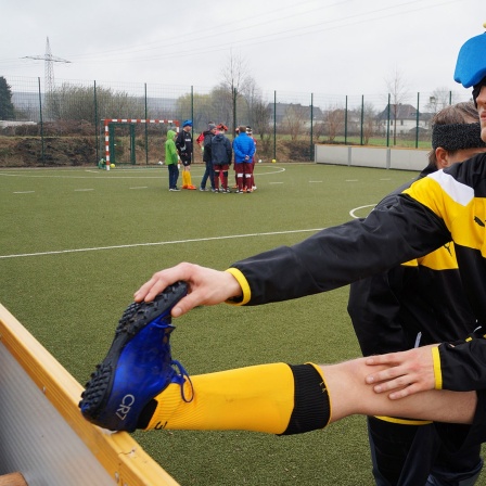 Fußballspieler mit verbunden Augen dehnt sein linkes Bein am Spielfeldrand.