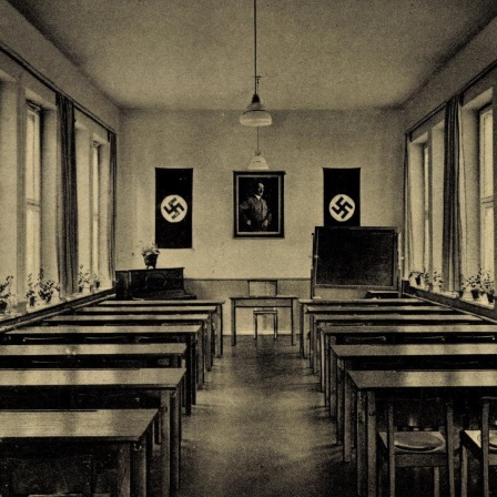 Eine Schwarzweißpostkarte zeigt in Zentralperspektive einen langgestreckten Sitzungssaal mit Reihen von Pulten jeweils an der rechten und der linken Seite des Raumes. Am Kopfende sind zwei Hakenkreuze und ein Führerbild, das Adolf Hitler abbildet, zu se