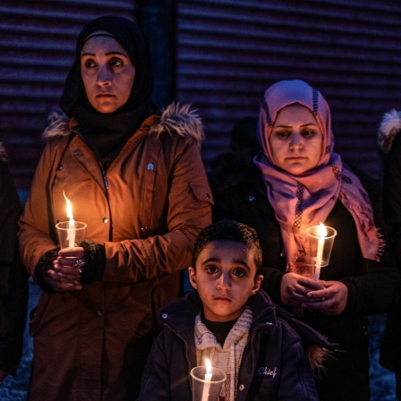 Zwei Frauen und ein Junge trauern mit Kerzen in den Händen.