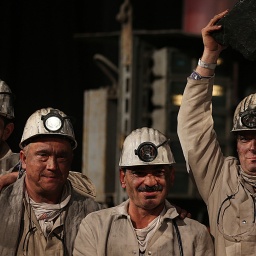 Bergleute stehen nebeneinander mit dem letzten Stück Steinkohle in der Hand.