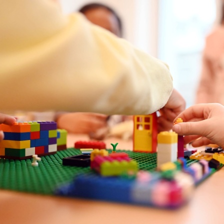 In einer Kita spielen Kinder an einem Tisch mit kleinen Bauklötzen
