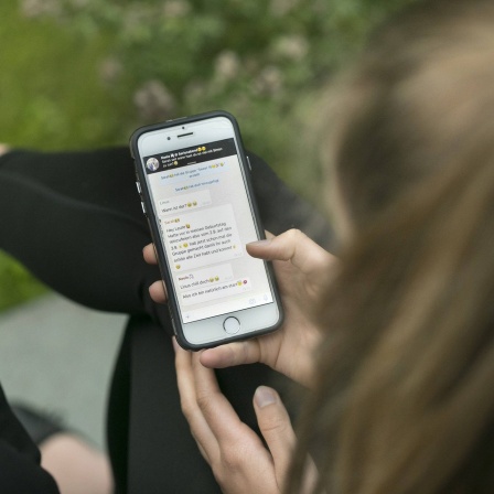  Jugendliche betrachtetn den Verlaut eines Chats mit Freunden auf ihrem Smartphone.